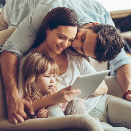a family of three huddled together while looking at a tablet device