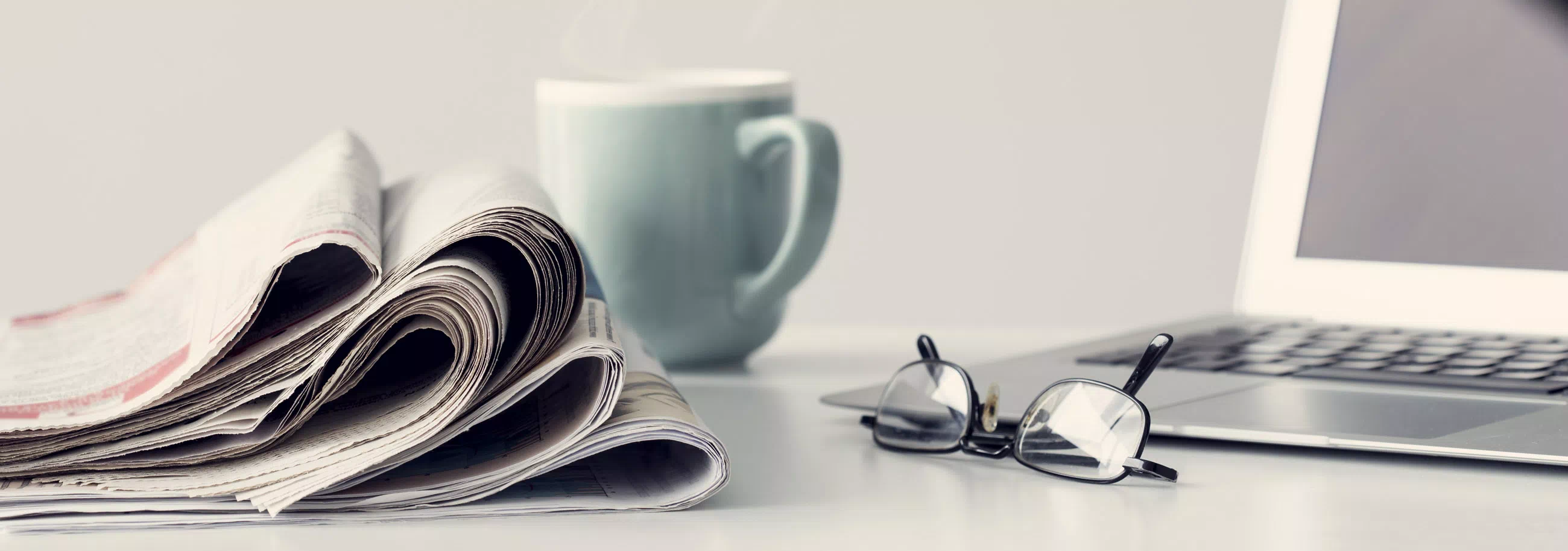 newspapers, reading glasses, a pen, and a cup of coffee on a table