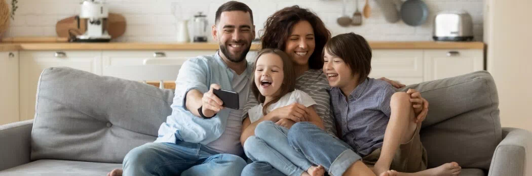 a family of four huddled together in a living room looking at a mobile device